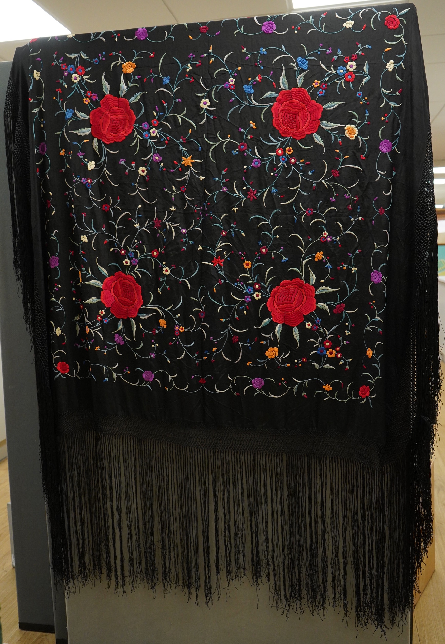 A late 19th century Chinese black silk polychrome floral embroidered shawl with long silk fringing. Embroidered with large red roses and an all over multi coloured floral sprig design. 123cm x 108cm. Condition, silk and
